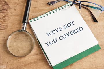 Text sign showing We Ve Got You Covered on a notebook with a magnifying glass and glasses on a...
