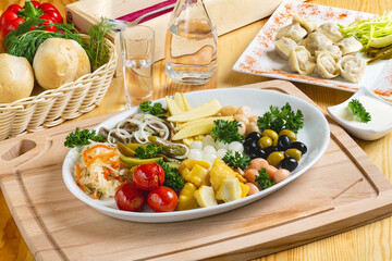 Assorted snacks to go with vodka: pickles, tomatoes, olives, mushrooms, sauerkraut on a plate, lunch, cafe.