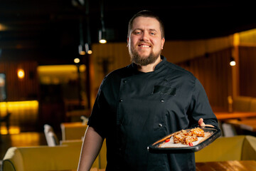 in a restaurant a chef in a black jacket stands smiling with a prepared Chicken wings