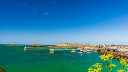 Panorama of Saint-Malo, the Breton corsair city. Seen from the ramparts and the port entrance, under a blue sky. - obrazy, fototapety, plakaty