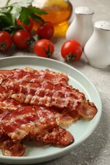 Plate with fried bacon slices, tomatoes, spices and parsley on grey textured table, closeup