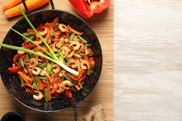 Shrimp stir fry with vegetables in wok and ingredients on wooden table, flat lay. Space for text