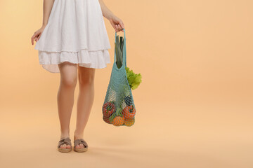 Woman with string bag of fresh vegetables on beige background, closeup. Space for text