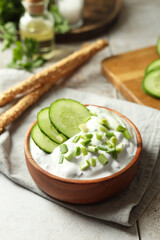 Delicious yogurt, green onion, cucumbers and grissini on table, closeup