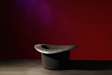 Magician's hat on black wooden table against color background, space for text