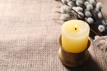 Burning church candle and willow branches on beige cloth, closeup. Space for text