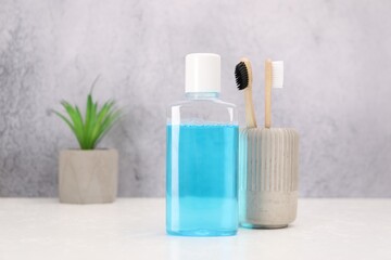 Bottle of mouthwash and toothbrushes on white table in bathroom