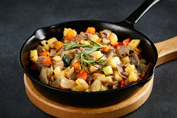 Savory cast-iron skillet ragout with tender meat and colorful vegetables on a textured black table