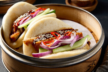 Authentic Asian cuisine: Bao buns with duck and vegetables in a steamer on a black table