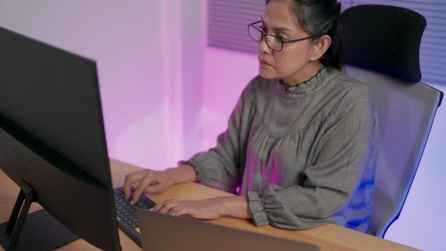 Freelance web designer sitting at desk in evening working, wondering about abnormal behavior of code on laptop computer, writing javascript binary code on workstation at work