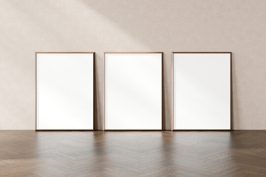 Three empty vertical picture frames leaning against a textured wall, placed on a herringbone pattern wooden floor, 3d render.