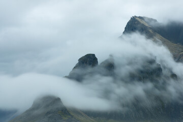 Atmospheric Clouds breaking over the ridge of Vestrahorn mountains on a overcast day in Stokksnes,...