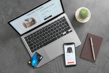 Online store website on laptop screen. Computer, smartphone, stationery, credit card and cactus on grey table, flat lay