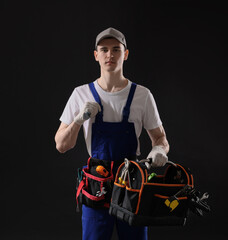 Professional repairman with tool box on black background