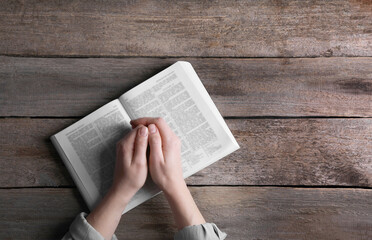 Religion. Christian woman praying over Bible at wooden table, top view. Space for text