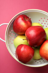 Colander with fresh apples on pink table, top view