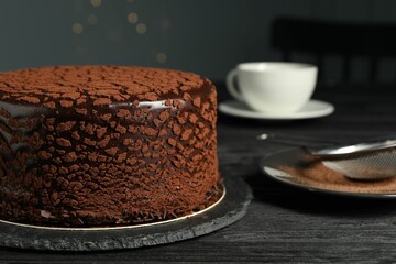 Delicious chocolate truffle cake and cocoa powder on black wooden table, closeup