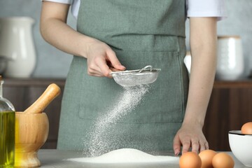 Woman sieving flour at table in kitchen, closeup