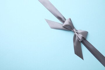 Grey satin ribbon with bow on light blue background, top view