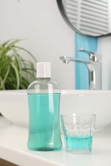 Bottle of mouthwash and glass on white table in bathroom