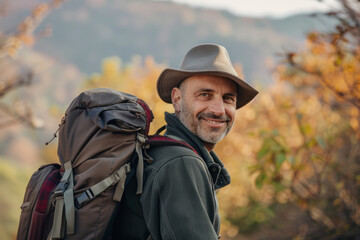 Smiling hiker with a hat looking over his shoulder amidst autumn foliage.