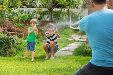 Happy children playing with water pistols against their father