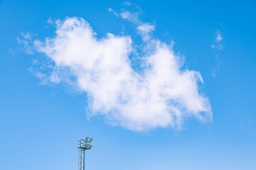 Fluffy white clouds in a clear blue sky with a light pole