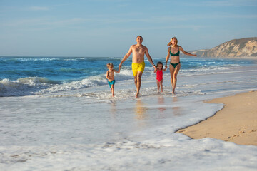 A happy family enjoying sunny day at run in foamy wave on beach