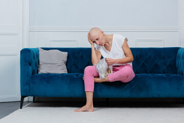 Bald woman sits distressed on couch tired of chemo treatment