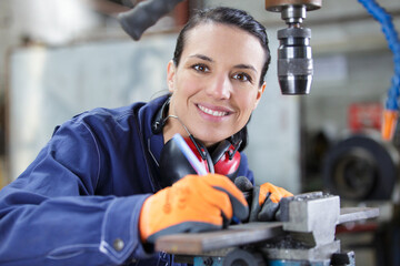 female apprentice using drill in factory