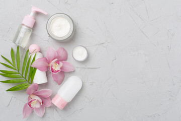 Bottles and jars with cream and orchids on concrete background, top view