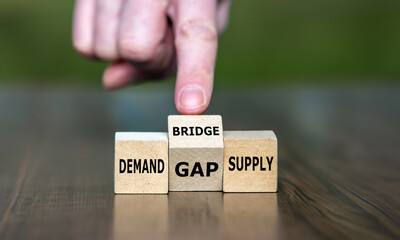 Hand turns cube and changes the word 'gap' to 'bridge' between the two words demand and supply. Symbol for closing the gap between a demand and the supply.