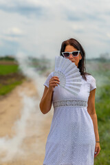 woman is holding a white fan in her hand while walking on a dirt road