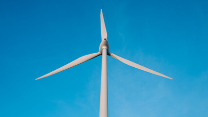 A wind turbine is standing tall in the sky, with the blue sky behind it