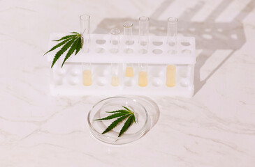 Laboratory test tubes with yellow liquid and a round glass medical container with a cannabis leaf...