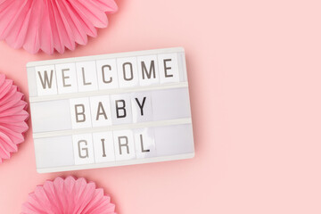 Welcome baby girl. Lightbox with letters and tissue paper fans in a pink color. Concept with place...