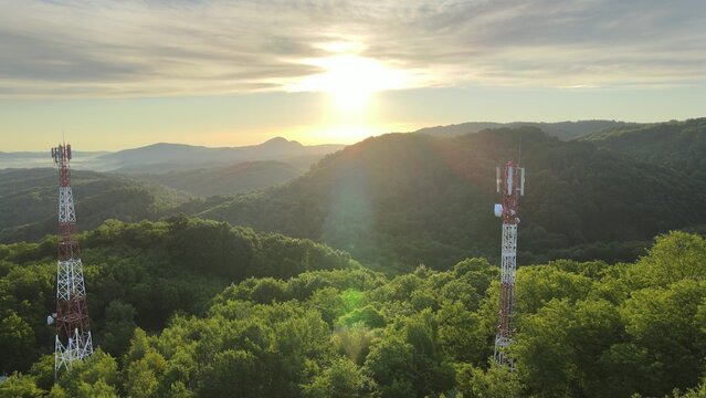 Aerial view of 5G telecom tower antenna for data internet wireless smartphone generation. Drone shoot in the middle of a green forest during an epic sunrise in a mountain landscape
