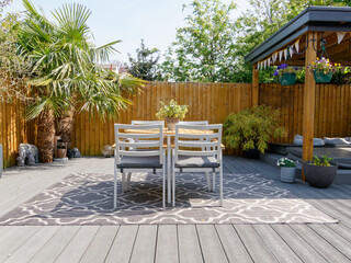 Minimalistic English modern garden with table and chairs. Sunny summers day with green plants and decking on the patio