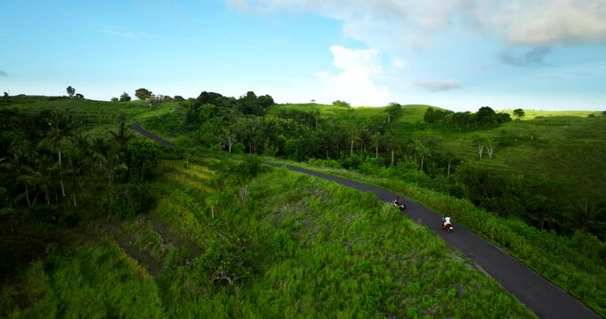 Girl on scooter explores lush landscape of Teletubbies Hills, Nusa Penida. Drone