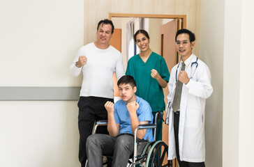 Doctor and nurse encourage father and boy patient on wheelchair in hospital