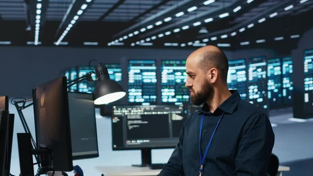 System operator overseeing server room, typing code on desktop PC, troubleshooting rigs. Software specialist doing maintenance on hardware clusters, networking systems and storage arrays