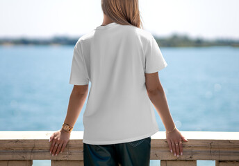 Mockup of a textured white t-shirt on a blonde girl in leather pants, on the embankment, back view of the shirt, for design, branding.