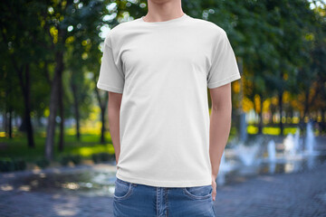 Mockup of a white fashion T-shirt on a man in jeans, front view, on the background of a park, fountain.