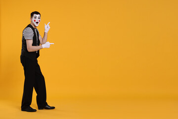 Funny mime artist pointing at something on orange background. Space for text