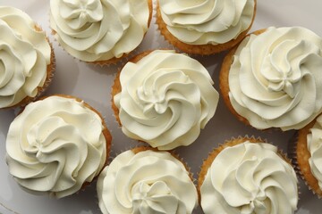 Tasty vanilla cupcakes with cream on plate, flat lay