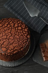 Delicious truffle cake, server and chocolate pieces on black wooden table