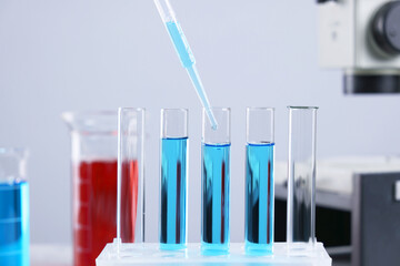 Dripping liquid from pipette into test tube on blurred background, closeup