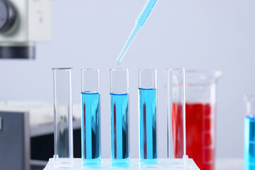 Dripping liquid from pipette into test tube on blurred background, closeup