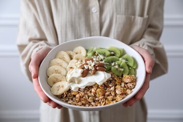 Woman holding bowl of tasty granola indoors, closeup