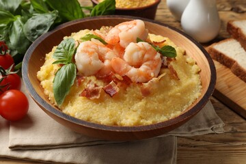 Fresh tasty shrimps, bacon, grits and basil in bowl on wooden table, closeup